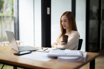 Businesswoman sitting and enjoying hot coffee, pay attention on the laptop screen while relaxing.