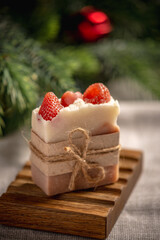 Beautiful fragrant piece of berry natural soap on an organic wooden soap dish against the background of the green branches of the Christmas tree