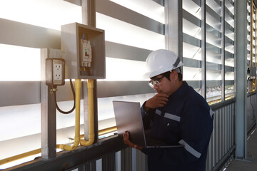Chief engineer in hard hat walks through modern factory lighting while holding laptop. Successful handsome man in modern industrial environment.