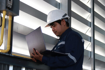 Chief engineer in hard hat walks through modern factory lighting while holding laptop. Successful handsome man in modern industrial environment.