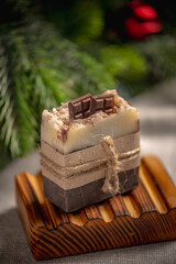 Beautiful fragrant piece of chocolate natural soap on an organic wooden soap dish against the background of the green branches of the Christmas tree