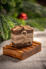 Fragrant brown piece of natural soap on an organic wooden soap dish against the background of the green branches of the Christmas tree