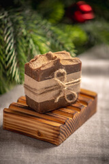 Fragrant brown piece of natural soap on an organic wooden soap dish against the background of the green branches of the Christmas tree
