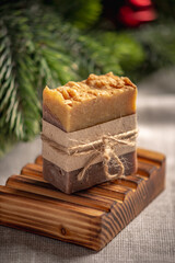 Fragrant yellow brown piece of natural soap on an organic wooden soap dish against the background of the green branches of a coniferous tree