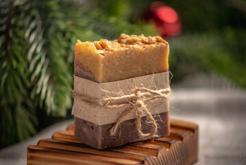 Fragrant yellow brown piece of natural soap on an organic wooden soap dish against the background of the green branches of the Christmas tree