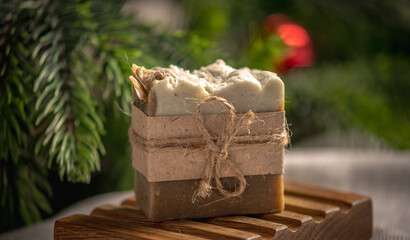 Fragrant piece of natural coniferous soap on an organic wooden soap dish against the background of the green branches of the Christmas tree