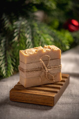 Fragrant yellow piece of natural soap on an organic wooden soap dish against the background of the green branches of a coniferous tree