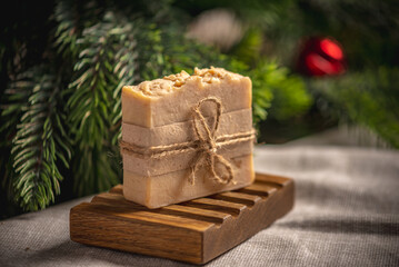 Fragrant yellow piece of natural soap on an organic wooden soap dish against the background of the green branches of the Christmas tree