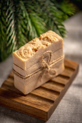 Fragrant yellow piece of natural soap on an organic wooden soap dish against the background of the green branches of a coniferous tree