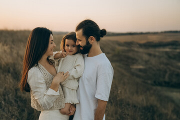 Happy family strolling in nature all together. Joyful mother, bearded father and little daughter walking on the field, noise effect