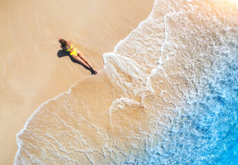Aerial view of the beautiful young lying woman on the tropical sandy beach near sea with waves at...