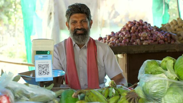 Vegetable vendor smiling towards the camera while sitting at his stall - fresh vegetables  small business  Indian . Man selling vegetables - posing for the camera  QR code scanner  measuring scale ...