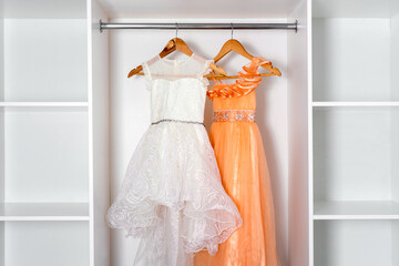 White and orange puffy dresses hang on hangers in modern white dressing room.