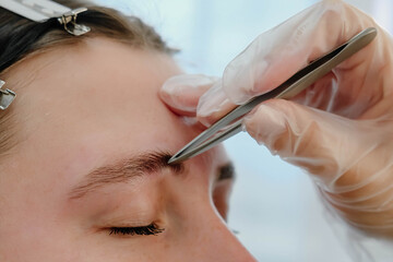 A makeup artist plucks a woman's eyebrows with tweezers. Beautiful thick eyebrows close-up