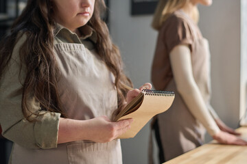 Cropped shot of young woman with Down syndrome writing down orders of clients in notepad while...