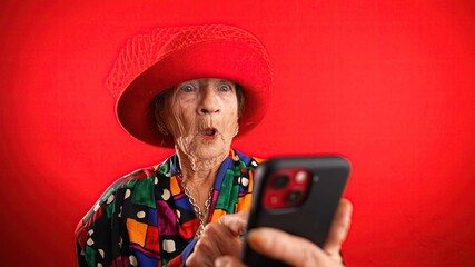 Portrait of toothless elderly senior old woman with wrinkled skin looking at phone having great...