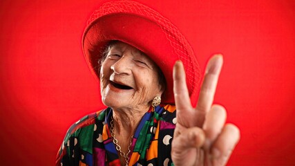 Happy fisheye portrait caricature of funny elderly woman with red hat giving peace sign gesture...