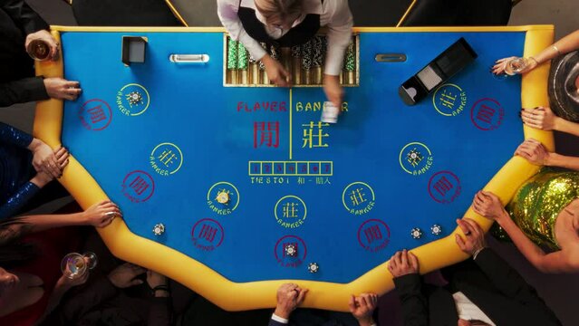 Top Down View Of Glamorous Casino Gamblers Placing Bets and Having Fun While Winning at Baccarat Table. Professional Croupier Dealing Cards, VIP People Enjoying Luxurious Lifestyle, Having Drinks.