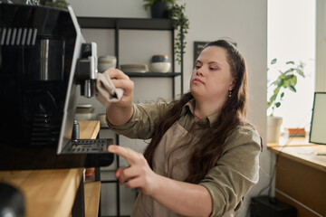 Young woman with mental disability wiping details of coffee machine with wet duster before preparing cappuccino for clients of cafe - obrazy, fototapety, plakaty