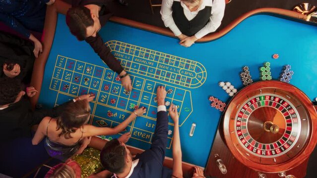 Top Down View Of Successful Men And Women Partying In A Luxurious Casino. Young People Gambling At A Roulette Table, Putting High Stakes Bets. Entertainment Industry And Glamorous Lifestyle Concept.