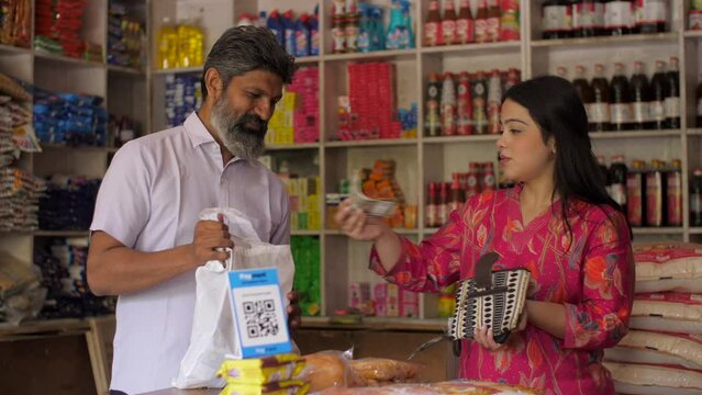 Indian woman giving cash money to the shopkeeper - purchasing groceries  kirana shop  small business  Indian store  selling fmcg products . A happy man selling groceries to a customer- buying and s...