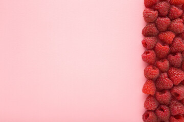 Row of fresh red raspberries on light pink table background. Pastel color. Closeup. Top down view....