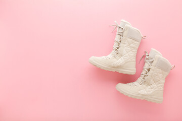 New beige warm winter boots with shoelace on light pink table background. Pastel color. Female footwear. Closeup. Top down view. - obrazy, fototapety, plakaty