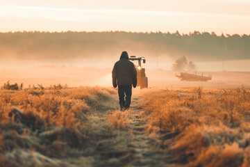 A farmer walking toward a tractor in a misty field during a beautiful sunrise in the countryside. - obrazy, fototapety, plakaty