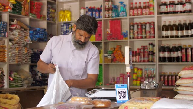 Grocery or kirana store shopkeeper packing groceries - e-commerce delivery  dark store  shopping bag  retail store  online business. Indian shopkeeper working at his shop - home delivery  online bo...