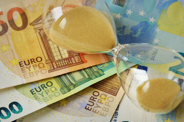 Close-up of hourglass lying on euro banknotes - Concept of time and money - 705717472