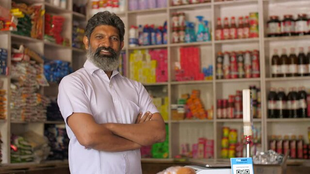 A portrait shot of a happy Indian grocery store owner posing at his retail shop - fmcg products. A successful Indian kirana or grocery businessman standing confidently with a smile - small business...