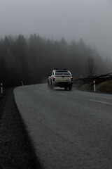 A car in the moody mountains. A car takes a bend in the misty mountain.