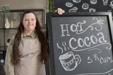 Young woman with Down syndrome standing by blackboard with special offer written with white chalk...