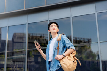 Portrait of handsome Asian student using smartphone. A young man standing outdoor happy smiling with holding mobile phone