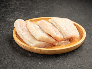 Portion of raw fresh white fish fillet in a wooden plate