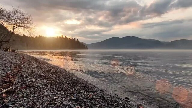 Serene scenic view of sunset Teletskoye Lake. Calm waves and fog above water.