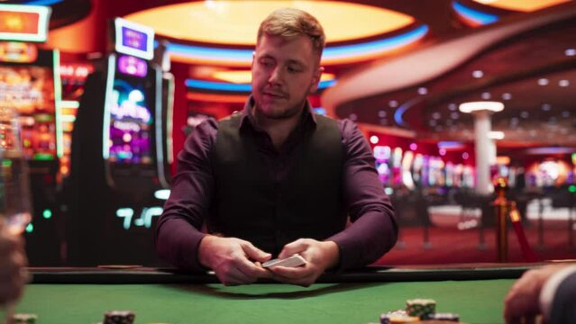 Caucasian Male Poker Croupier Dealing Cards To Young Couple. Zoom Out To Beautiful Woman In Fancy Dress Playing Against Handsome Man In Luxurious Casino. Gamblers Betting, Drink Champagne. Slow Motion
