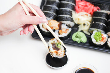 Sushi background. Woman hand holding chopsticks. Salmon calabash roll. Japanese food isolated on white table. Eating sushi with dark soy sauce. Takeaway sushi lunchbox. Dipping sushi in soy sauce.