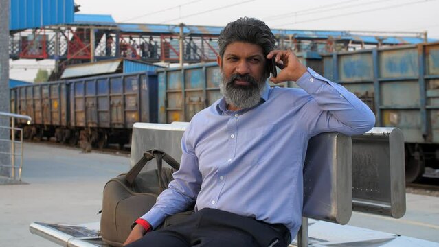 Faridabad  India  29 September  2023 - A middle-aged Indian man talking on phone at the railway station - waiting for train  railway platform. An Indian man waiting to start his train journey - goo...