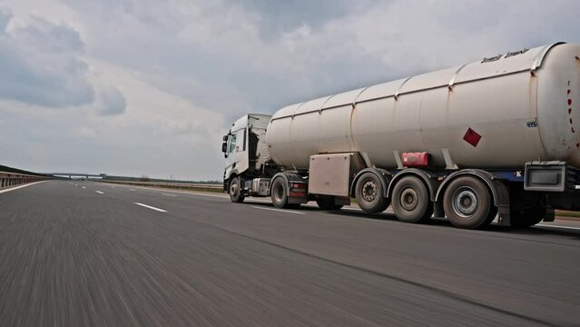Rolling shot of tank truck with gasoline, gas or other fuel, oil trailer driving on highway. Transportation by land, cargo and oil delivery