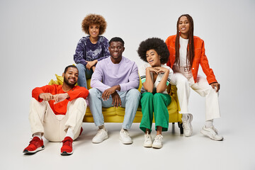 cheerful african american people in bright casual wear sitting together on yellow couch on grey