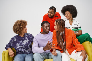 smiling african american friends in colorful casual attire chatting and sitting on yellow couch