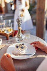 Delicious sweet dessert on a white porcelain plate. Meringue with blueberries lies in front of a woman. Female hands with white manicure hold a plate.