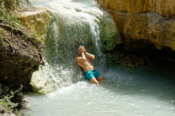 Man bathes in geothermal pool and thermal spring in Tuscany, Italy. Bagni San Filippo under the natural thermal waterfall of Mount Amiata. Known to tourists as the white whale
