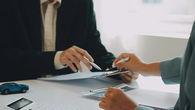 Salesman guiding customer seated at table. Car business. Car sale. Dealership closing. and the new owner has entered into a contract The idea of ​​selling and renting a car with insurance.
