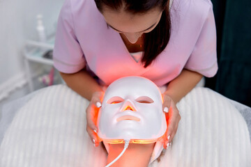 woman receiving led light therapy mask treatment from beautician in beauty salon