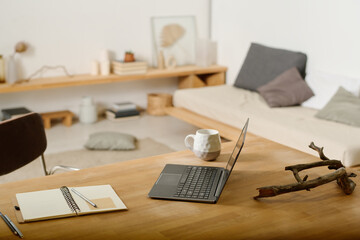 Workplace with laptop, open notepad with pencils and pen, cup of coffee or tea and decorative snag or driftwood on wooden table