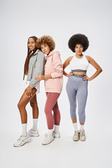 pretty african american female friends in sportswear looking at camera on grey backdrop, Juneteenth