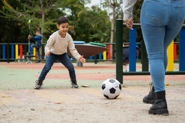 Close up low angle view of young mom and her little son playing soccer together outdoors in a public park