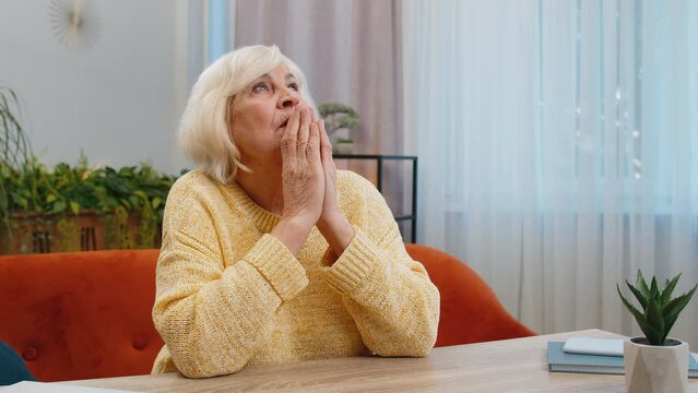 Please, God Help. Worried Senior Woman Praying For Heath Sincerely With Folded Arms, Looking Upward Making Wish, Asking Hopeful Imploring Expression Begging Apology At Home. Elderly Mature Grandmother